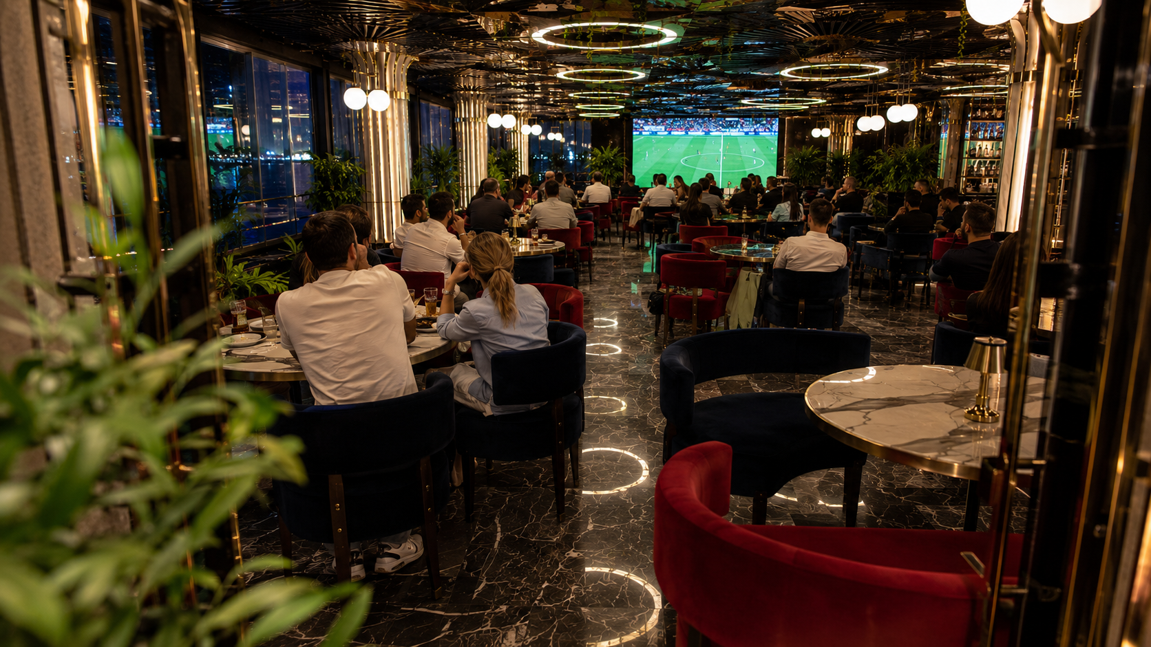 Küçükyalı ve Maltepe çevresinde modern restoranda büyük ekrandan futbol maçı izleyen kalabalık arkadaş gruplarının bulunduğu akşam atmosferi.