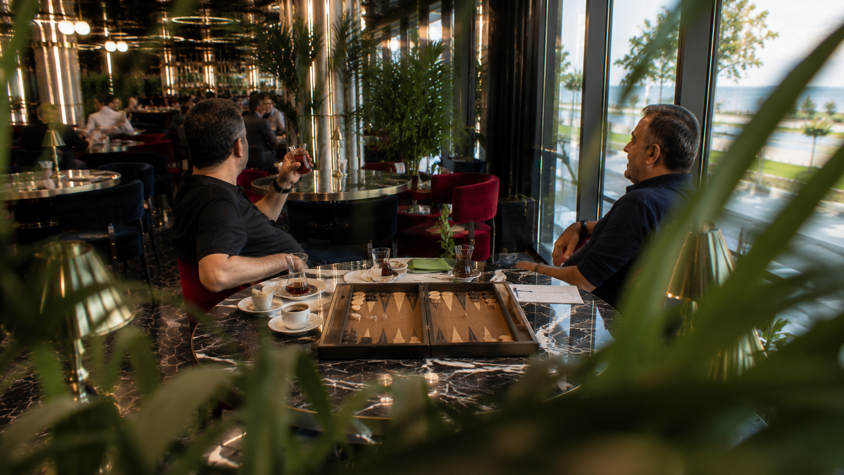 Küçükyalı'nda modern lounge ortamında tavla oyunu sonrasında sohbet eden iki arkadaşın huzurlu öğleden sonra atmosferi.